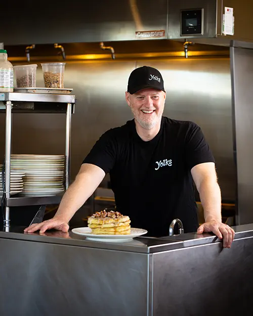 Yolks breakfast franchise employee smiling while presenting a stack of pancakes