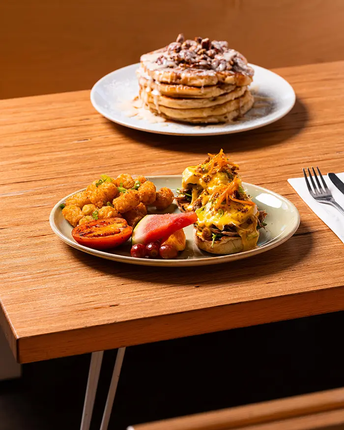 Breakfast combo with fluffy pancakes and eggs benedict served with roasted potatoes on wooden table