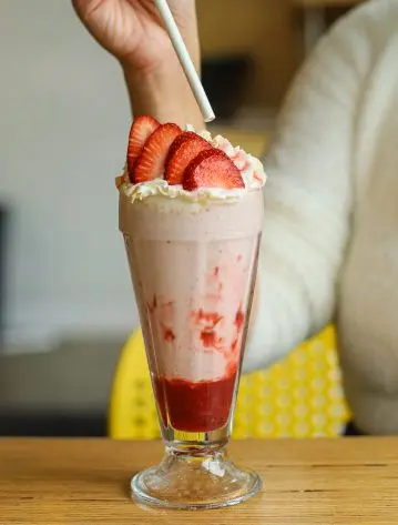 Strawberry milkshake topped with whipped cream and fresh strawberries in a tall glass