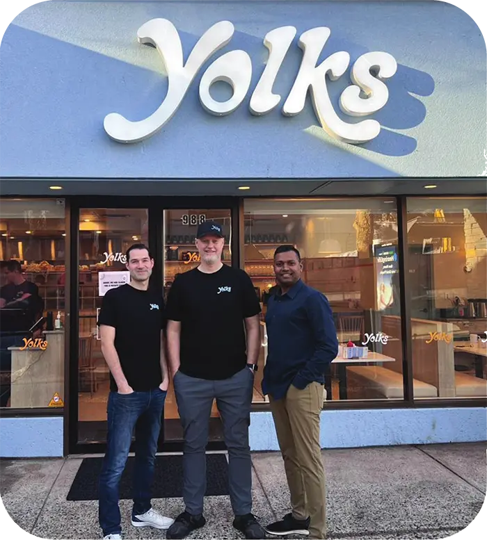 Yolks team standing in front of one of their restaurants with a YOLKS sign above them