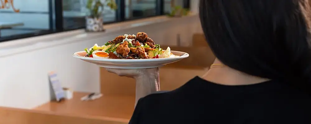 Server carrying a plated brunch dish in a restaurant, representing a breakfast franchise Canada concept