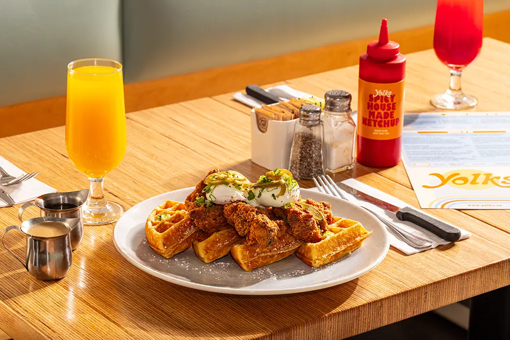 Chicken and waffles breakfast with crispy fried chicken, golden waffles, and poached eggs at Yolks.